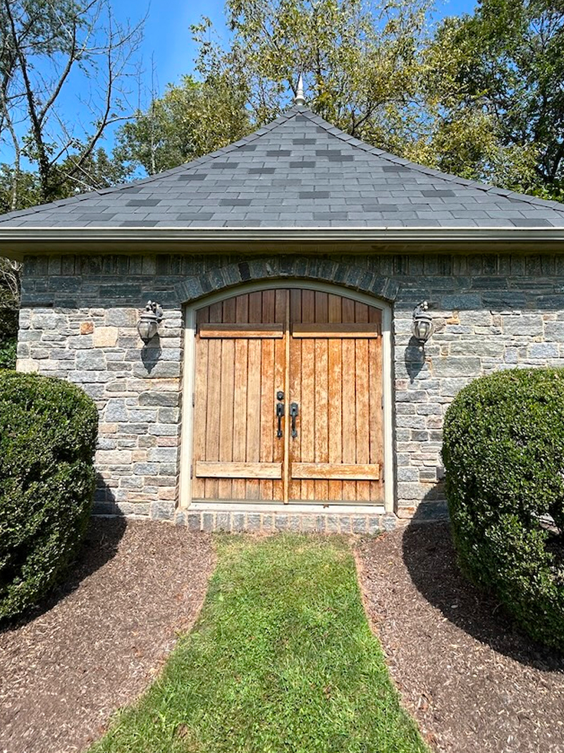 Exterior wood doors after staining — rich walnut finish on stone carriage house